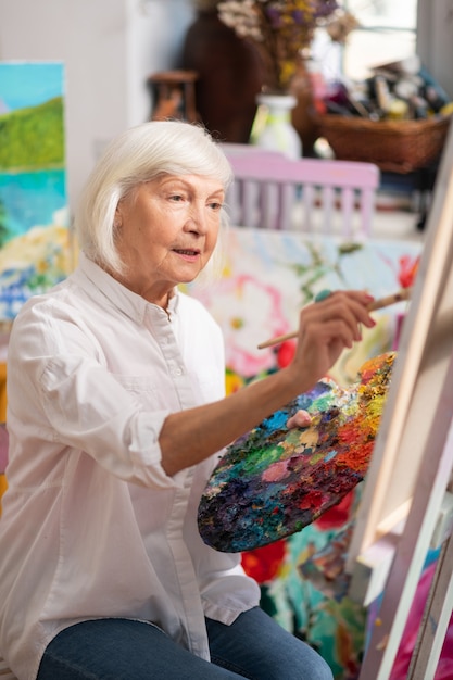 Sentarse y pintar. Vista superior de la anciana rubia sentada cerca de la lona con paleta de colores