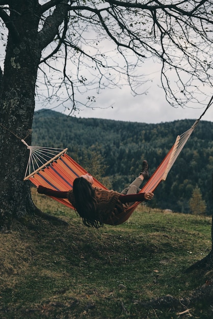 Sente a liberdade. bela jovem deitada na rede enquanto relaxa no vale debaixo da árvore
