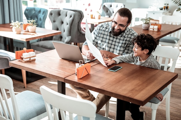 Sente-se à mesa. Pai e filho elegantes e bonitos sentados à mesa em um restaurante escolhendo pratos