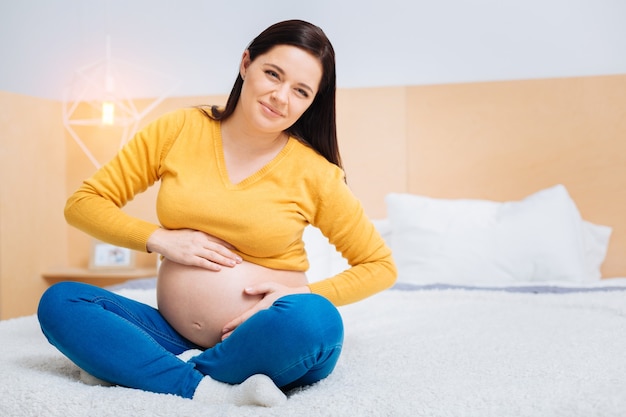 Sentimentos estranhos. Mulher morena atraente pressionando os lábios enquanto toca sua barriga e olha para o lado