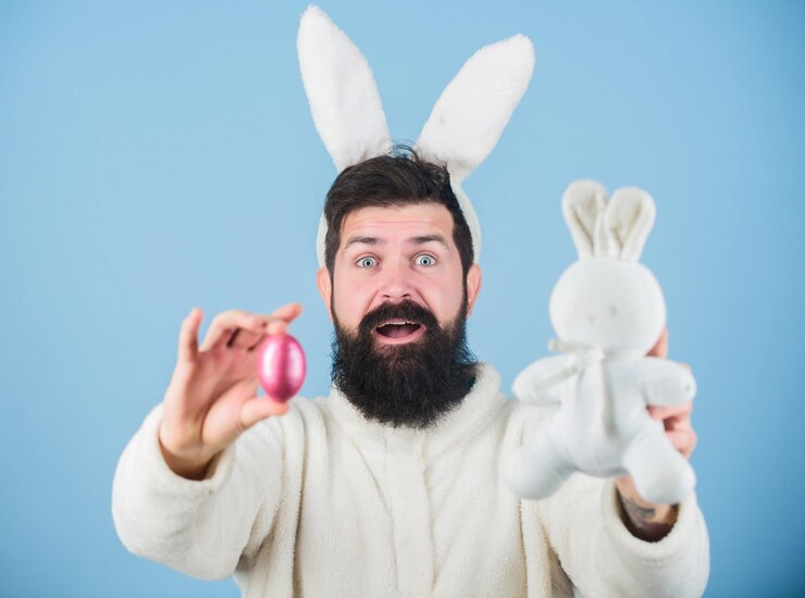 Foto sentindo-se animado com a páscoa hipster com longas orelhas de coelho segurando a lebre poedeira de ovos coelhinho da páscoa entregando ovos coloridos celebração do feriado de primavera homem barbudo com brinquedo de coelho e ovo de páscoa