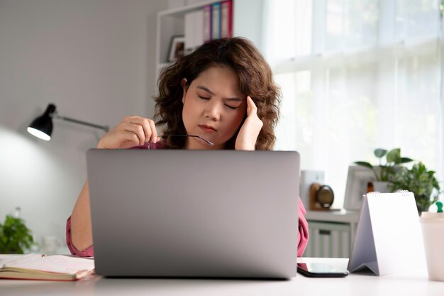 Sentindo-se cansado e estressado. Jovem empresária asiática sentada com os olhos fechados por exaustão e cansaço durante o trabalho em casa usando laptop. Trabalhadora asiática cansada e sobrecarregada, mas
