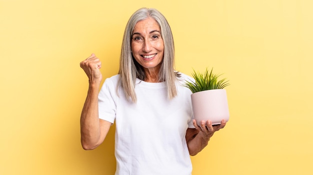 Sentindo-se chocado, animado e feliz rindo e comemorando o sucesso dizendo uau segurando uma planta decorativa