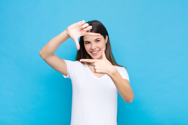 sentindo-se feliz, amigável e positivo, sorrindo e fazendo um retrato ou moldura com as mãos