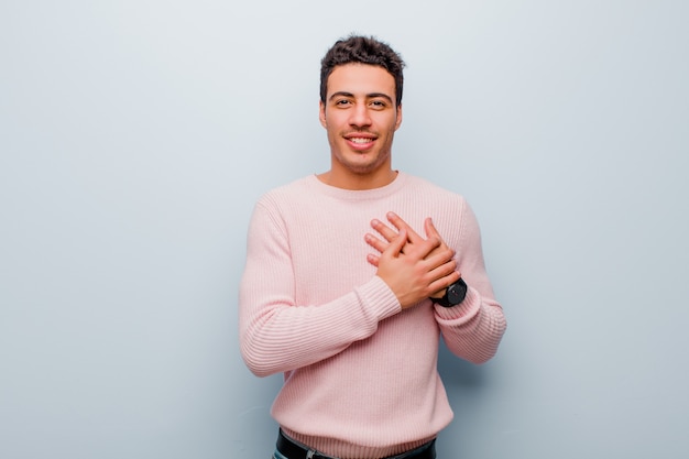 sentindo-se romântico, feliz e apaixonado, sorrindo alegremente e segurando as mãos perto do coração