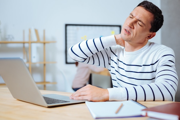 Sentindo-se sem esperança. Morena séria mantendo os olhos fechados enquanto está sentada em frente ao laptop e descansando no intervalo