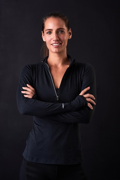 Sentirse bien y verse bien Retrato de estudio de una mujer joven en ropa de gimnasia de pie con los brazos cruzados sobre un fondo oscuro