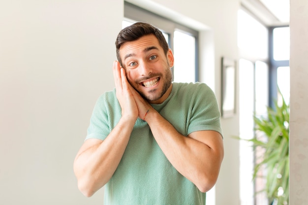 Sentirse enamorado y lucir lindo, adorable y feliz, sonriendo románticamente con las manos al lado de la cara.