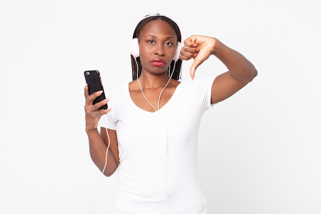 Sentirse enfadado, mostrando los pulgares hacia abajo con auriculares y un teléfono inteligente.