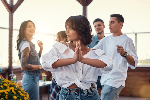 Foto sentirse feliz y pacífica mujer joven y bonita con camisa blanca está sosteniendo las palmas juntas