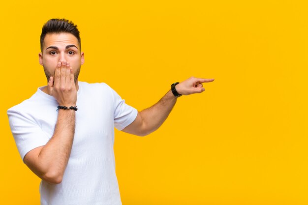 Foto sentirse feliz, sorprendido y sorprendido, cubriéndose la boca con la mano y señalando el espacio de copia lateral