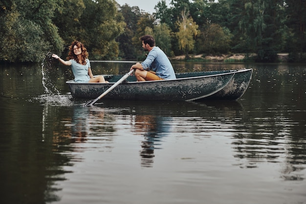 Sentirse juguetón. Hermosa joven pareja disfrutando de una cita romántica mientras rema en un bote