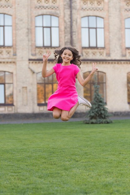 Sentirse libre. Salto de felicidad. La pequeña niña salta sobre la hierba verde. Llena de energía. Chica activa siente libertad. Diviértete y relájate. Niño despreocupado en vacaciones de verano. Adolescente en vestido rosa. Niña saltando al aire libre.