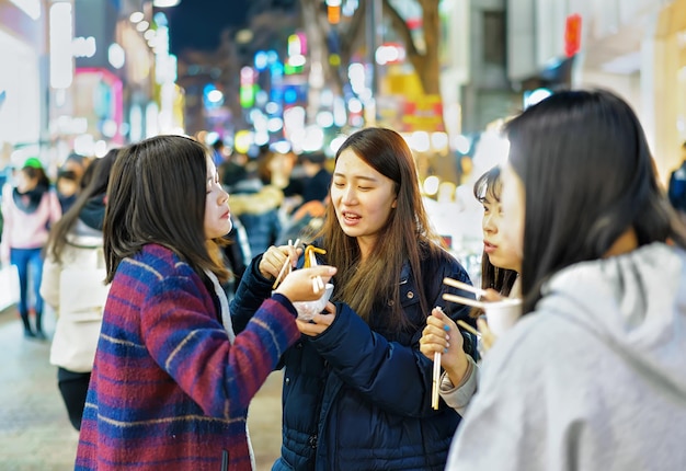 Seoul, Südkorea - 14. März 2016: Koreanische Mädchen probieren Street Food auf dem offenen Straßenmarkt Myeongdong, Seoul, Südkorea