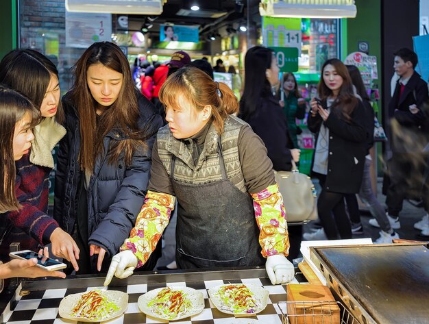 Seoul, Südkorea - 14. März 2016: Verkäufer und junge Käufer von Straßenlebensmitteln auf dem Myeongdong-Straßenmarkt in Seoul, Südkorea