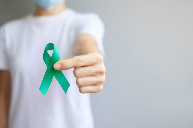 Septiembre Mes de concientización sobre el cáncer de ovario, mujer sosteniendo una cinta de color verde azulado para apoyar a las personas que viven y padecen enfermedades. Conceptos de salud y día mundial contra el cáncer