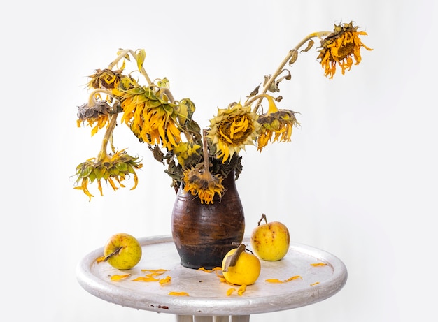 Seque el ramo de girasoles en florero y manzanas sobre la mesa. Bodegón de otoño