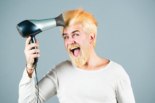 Seque seu cabelo. Barbudo divertido jovem segurar o cabelo seco isolado no fundo cinza, retrato de estúdio. Conceito de procedimentos de tratamento capilar. Simule o espaço da cópia.