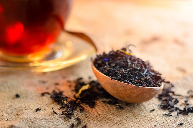 Seque el té negro en una cuchara de madera y una taza de té elaborado fragante en el fondo