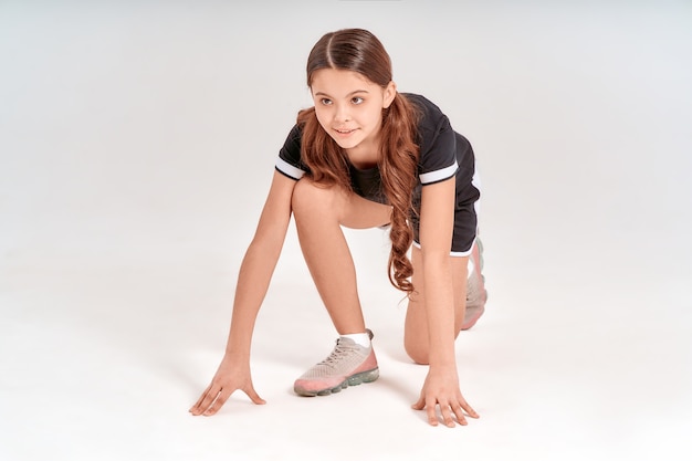 Ser ativo de comprimento total de uma linda garota adolescente em roupas esportivas, em pé na posição inicial e sorrindo