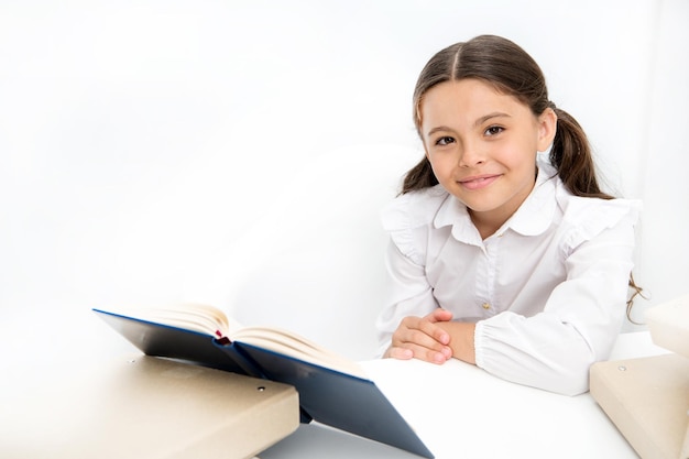 Ser inteligente e fofo. Criança pequena em idade escolar tem aula de literatura. Menina lendo livro de aula na escola. Colegial lendo livro escolar na mesa. Aluno adorável desenvolve habilidades de leitura.