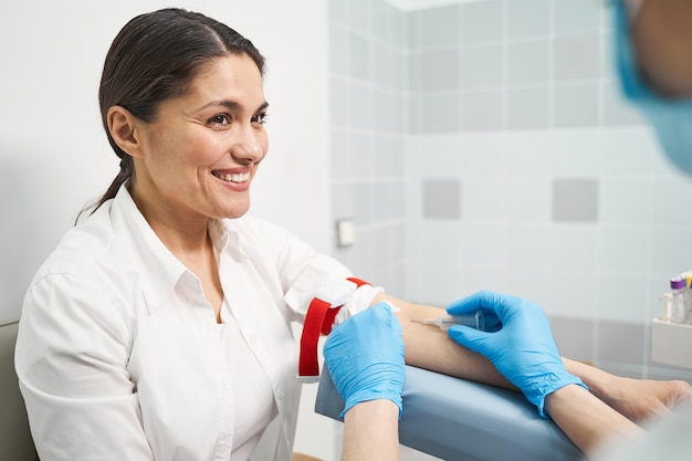 Ser positivo. Amable paciente joven que mantiene una sonrisa en su rostro mientras hace un puño durante la toma de muestras de sangre.