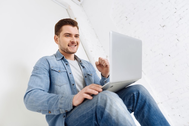 Ser positivo. Macho alegre manteniendo una sonrisa en su rostro y haciendo puño mientras está muy contento