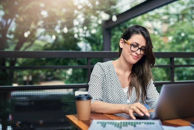 Ser produtivo fora do escritório Foto recortada de uma jovem empresária atraente trabalhando em seu laptop enquanto está sentada ao ar livre em um café
