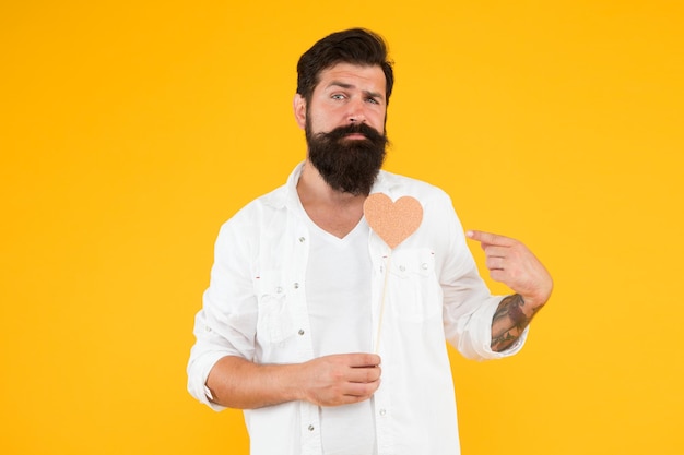 Seré tu Valentín. Saludo romántico. hombre con barba y bigote pared amarilla. Corazón hecho a mano para vacaciones. corazón de san valentín hipster brutal. fiesta del día de san valentín. hombre barbudo listo para la cita amorosa.