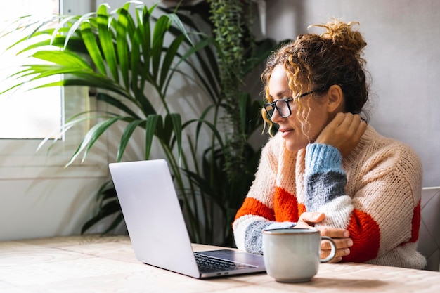 Serena joven mujer madura mirando y leyendo en el correo electrónico de notificación en línea de la computadora portátil Gente guapa que usa la computadora en casa relajándose sentada en la mesa sola Moderna actividad de ocio interior web