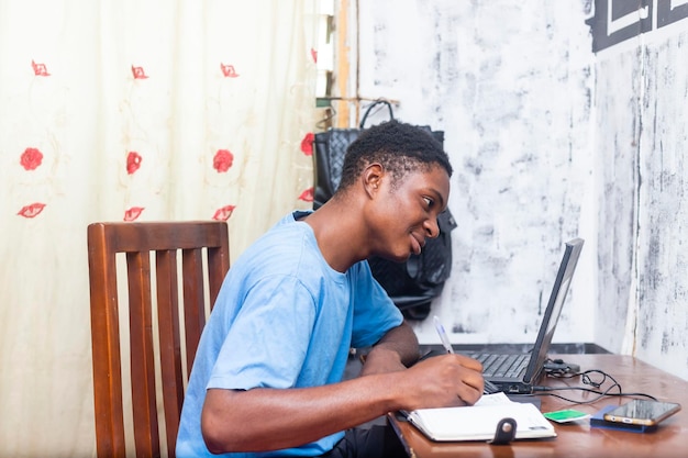 Serene jovem estudante negro africano em casa estudando online com laptop e escrevendo em um diário