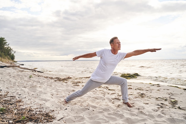 Sereno hombre deportivo está disfrutando de ejercicios de yoga en la orilla del mar y balanceándose en asana en la mañana