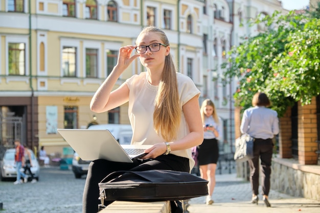 Séria jovem empresária em copos com laptop ao ar livre. Negócios, freelance, conceito de estilo de vida