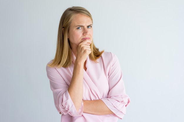 Seria mujer de negocios introspectivo tocar la barbilla y mirando a cámara.