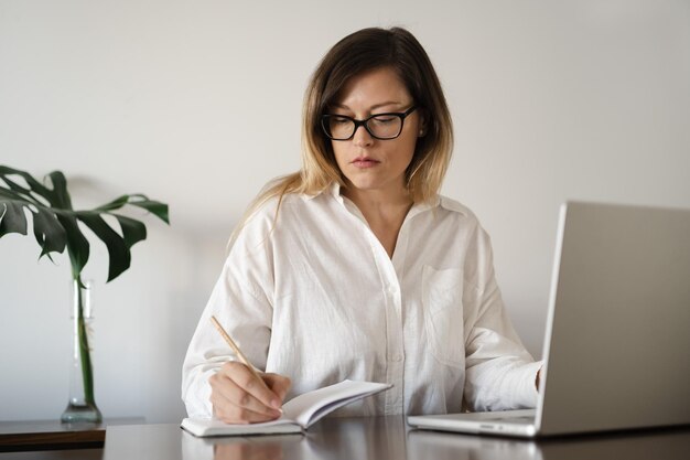 Seria mujer de negocios de mediana edad con gafas camisa de lino blanco con pelo largo y recto worki