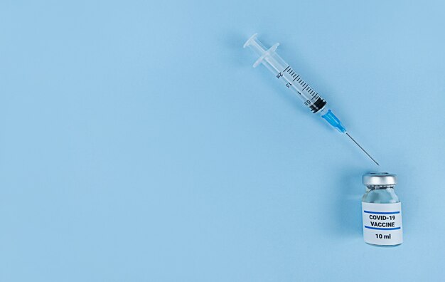 Seringa de uso único e frasco médico com vacina de coronavírus em um fundo azul com espaço de cópia.
