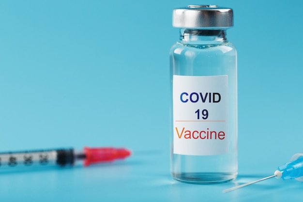 Seringa e ampola com vacina contra o vírus Covid-19 contra doenças em fundo azul.