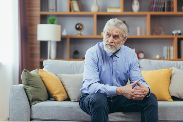 Serio para el abuelo pensativo sentado en el sofá en casa