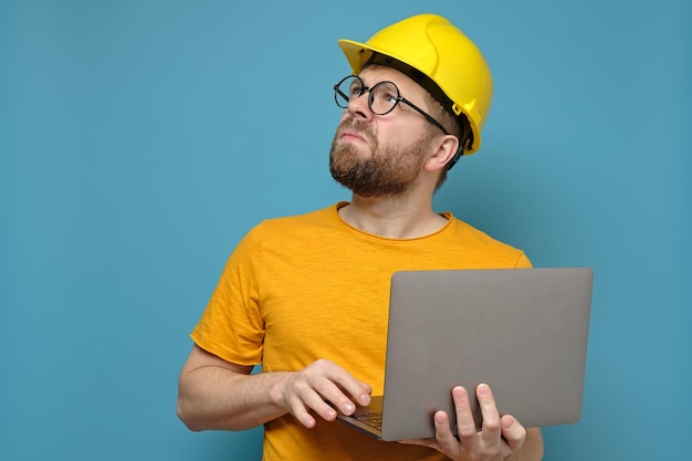 Serio capataz o ingeniero en casco de construcción se encuentra con una computadora portátil y mira hacia arriba