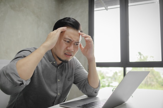 Sério cara de homem trabalhando no laptop sozinho na sala.