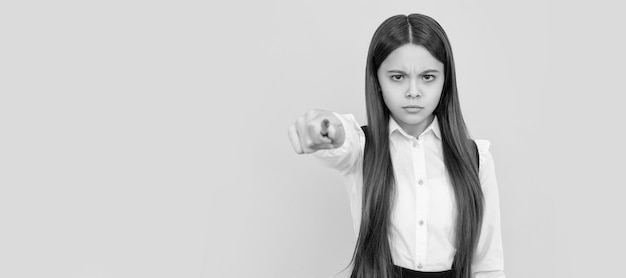 Foto serio ceño fruncido niña de la escuela apunta a la pluma sacando la mano fondo amarillo de vuelta a la escuela estandarte de la estudiante de la escuela retrato de la alumna de la escuela con espacio de copia