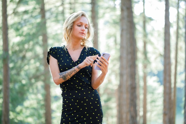 En serio, la chica bloguera está trabajando en el móvil en el fondo de la naturaleza