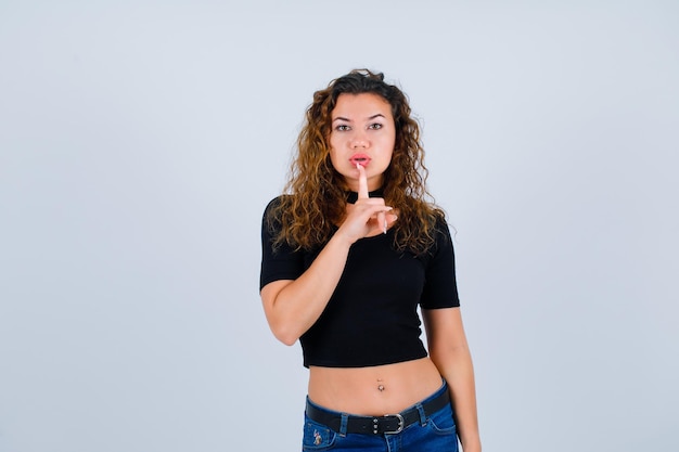 En serio, la chica sostiene el dedo índice en los labios sobre fondo blanco.