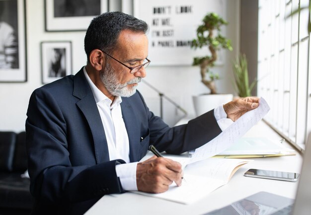 Serio concentrado caucásico empresario sénior en traje con tipos de contratos en la computadora en el moderno