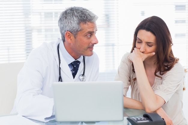 Serio docter mostrando algo en la computadora portátil a su paciente