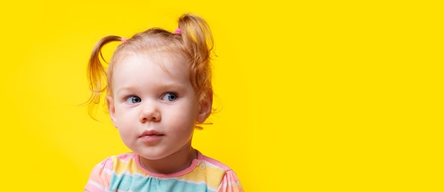 En serio, niña mirando de lado sobre fondo amarillo vacío, diseño panorámico con espacio para texto