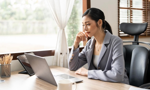 Seriöse Freiberuflerin, die online mit Buchhaltungsunterlagen auf einem modernen Laptop arbeitet Geschäftsfrau, die damit beschäftigt ist, im Büro am Laptop zu arbeiten