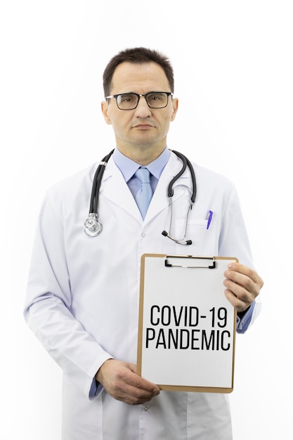 Seriöser Arzt zeigt Zwischenablage mit Inschrift Covid-19 Pandemic, medizinisch neu