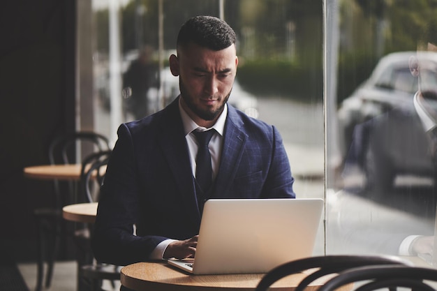 Seriöser asiatischer kasachischer Geschäftsmann, der mit einem Laptop in einem Café arbeitet