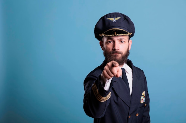 Seriöser Flugzeugflieger, der mit dem Finger auf die Kamera zeigt, Rekrutierung der Pilotenausbildung der Luftfahrtakademie. Selbstbewusster Finger mit Uniform der Flugbesatzung und Vorderansicht des Hutes